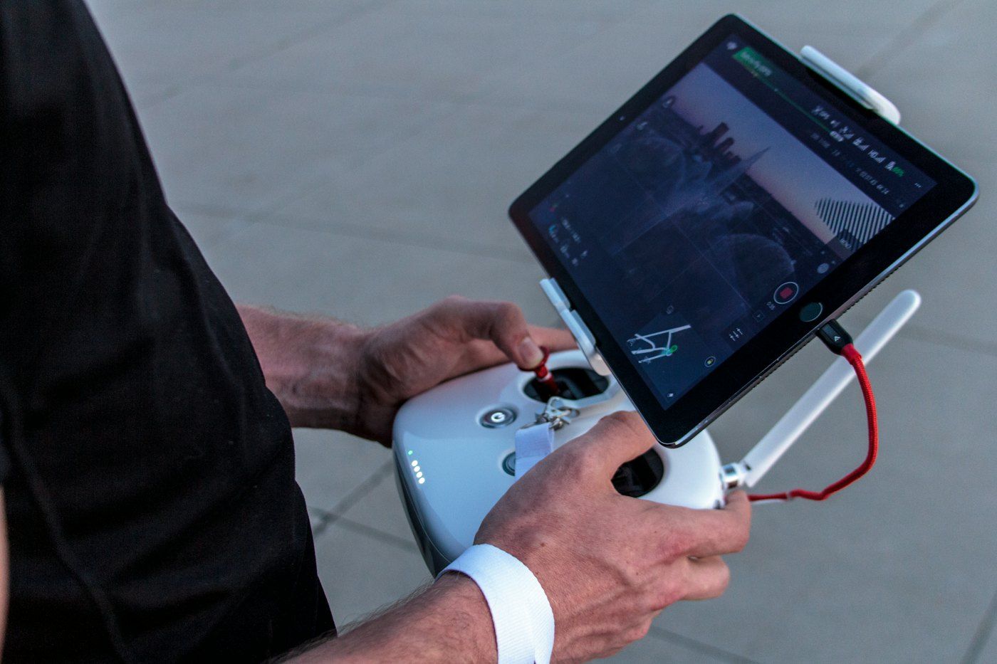A remote pilot holds a controller with a tablet showing the camera view.
